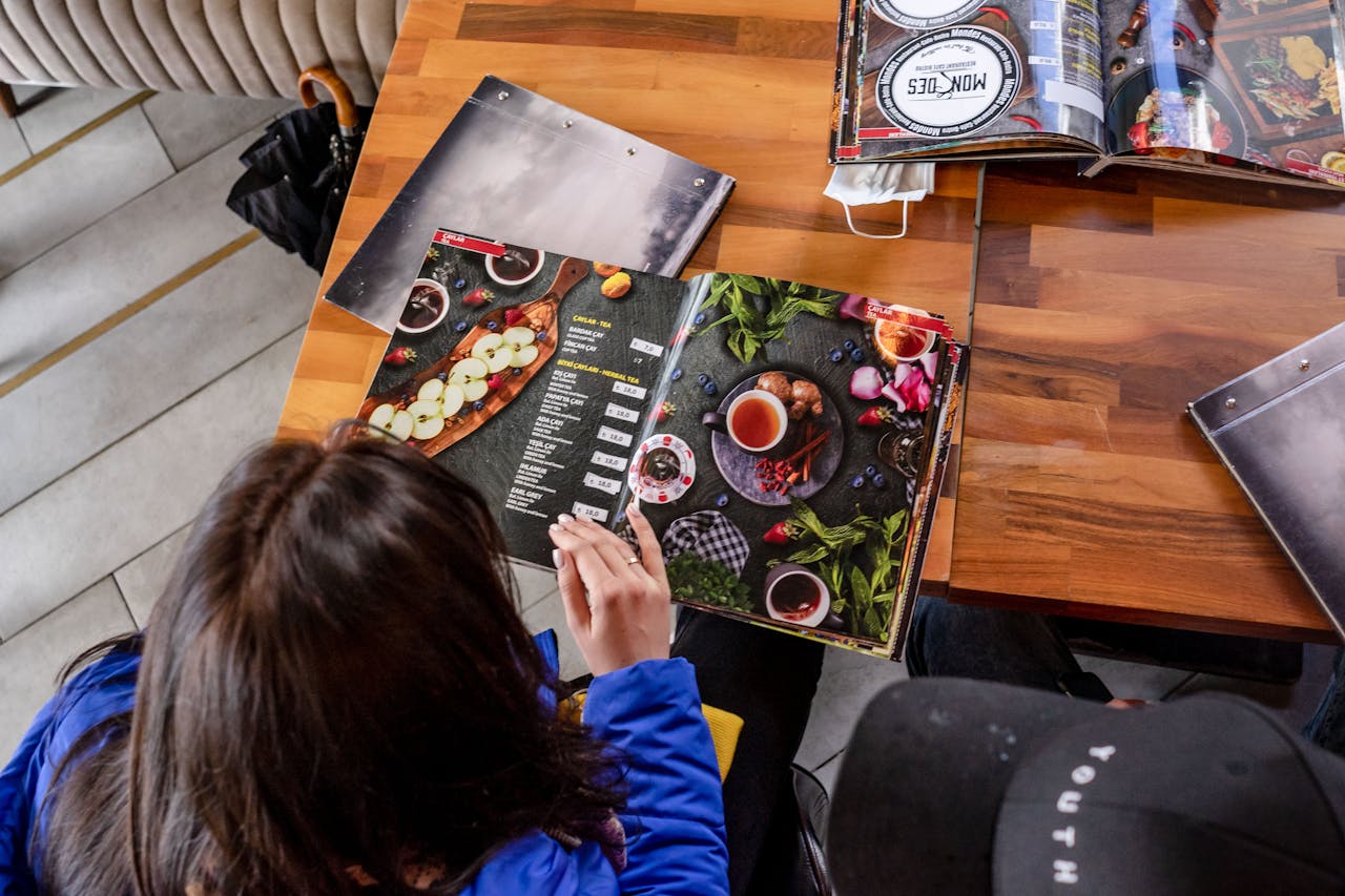 Two individuals explore food menus at a wooden table in a cozy café.